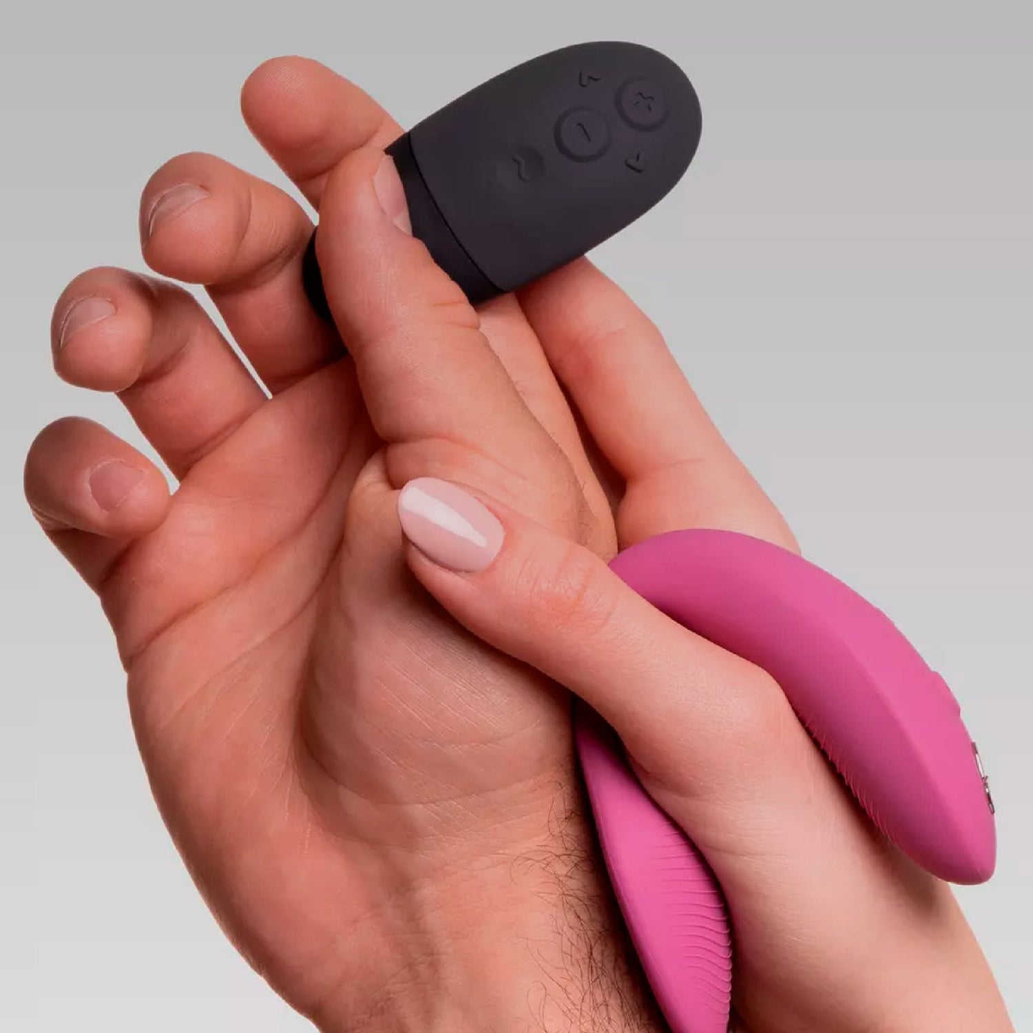 Close-up of two hands gently holding a pink remote-controlled vibrator and a black remote control, symbolizing intimacy and shared pleasure.