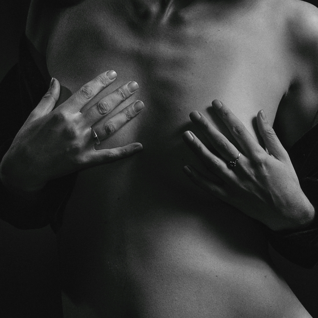 Close-up of a topless person in soft black-and-white lighting, covering their chest with their hands — capturing intimacy, vulnerability, and sensual self-expression.