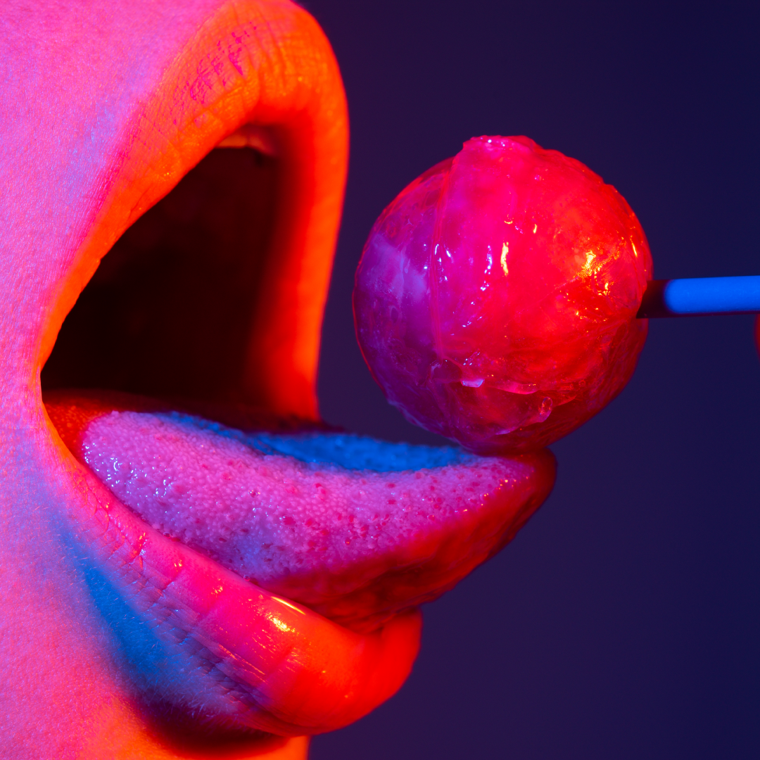 Close-up of lips and tongue about to taste a lollipop under neon lighting, symbolizing playful sensuality and sensory exploration