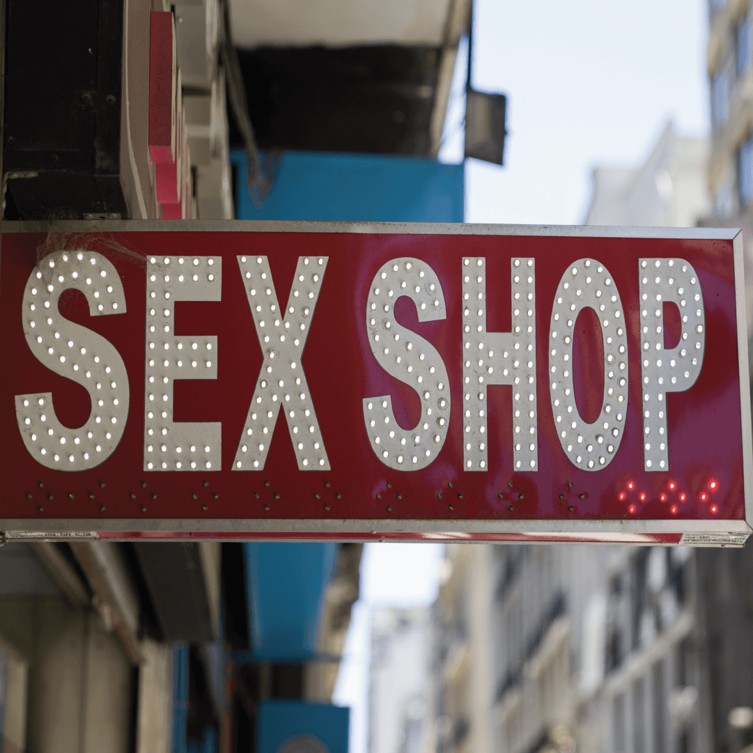 Illuminated red "Sex Shop" sign hanging above a busy city street