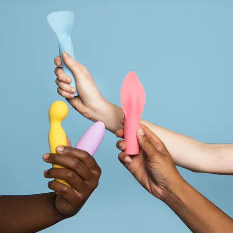 Four diverse hands holding colorful vibrators in pastel tones against a blue background, showcasing a variety of pleasure product shapes and designs.