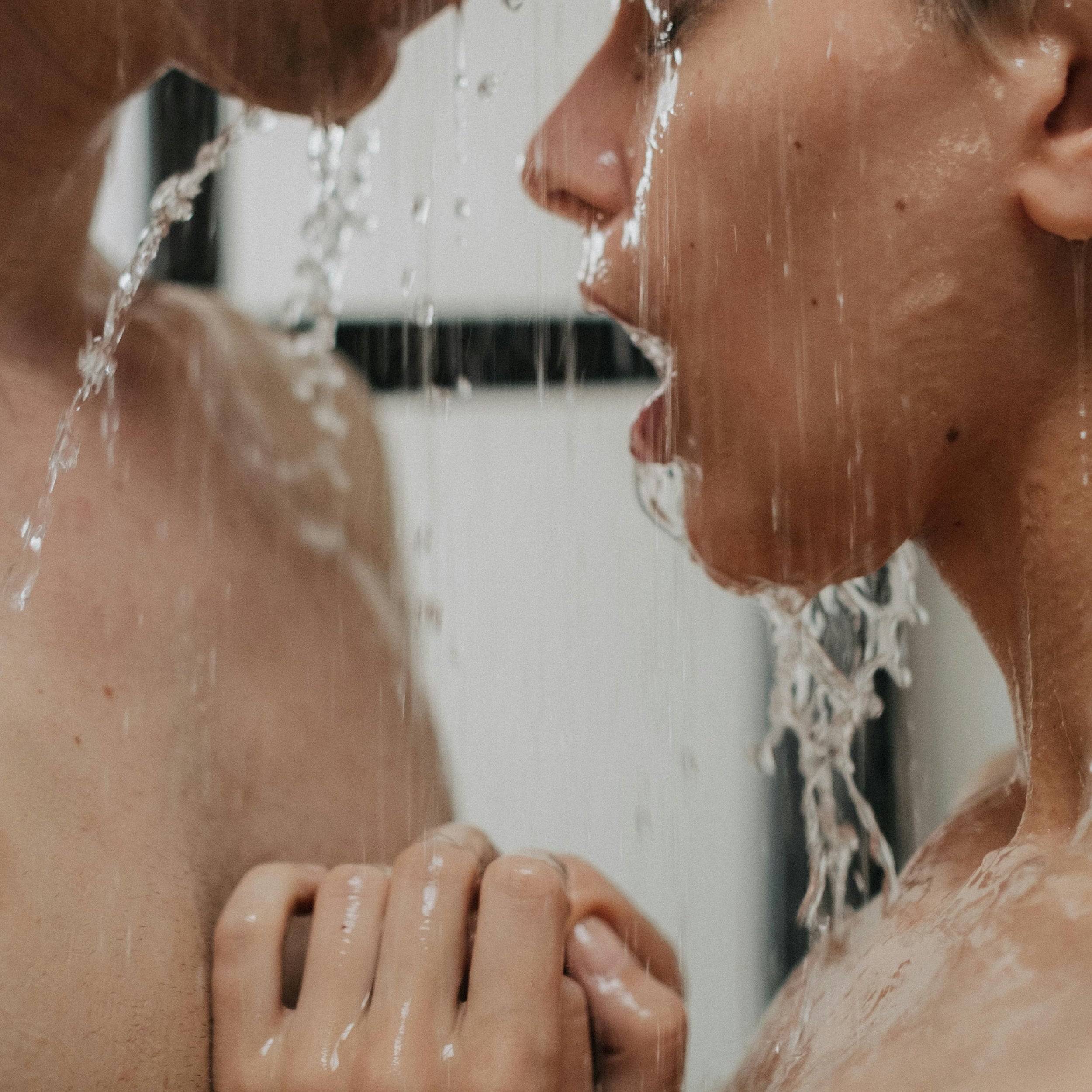Casal íntimo debaixo do duche, em momento sensorial de conexão e presença.